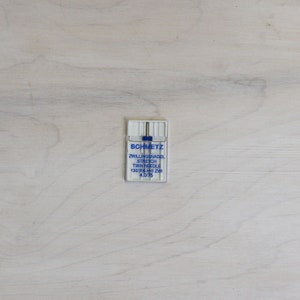 Pu&ograve; includere: Una confezione di plastica bianca contenente un paio di aghi gemelli Schmetz per tessuto elasticizzato. La confezione &egrave; etichettata "Zwillingsnadel Stretch Twin Needle 130/705 HS ZWI 4.0/75".
