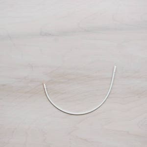 May include: A white wire or cord bent into a U shape, lying on a light wood surface.