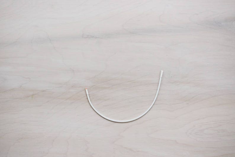 May include: A white wire or cord bent into a U shape, lying on a light wood surface.