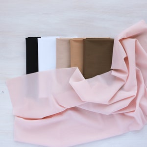 May include: A collection of fabric swatches in various shades of brown, beige, and white, with a pink sheer fabric draped over the top.