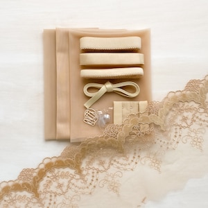May include: A set of beige fabric, lace, and elastic for sewing a garment. The set includes three pieces of elastic, a piece of lace trim, and a small bag of hardware.