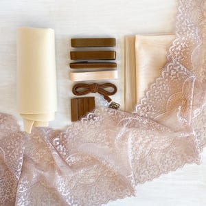 May include: A set of fabric and lace trim for sewing projects. The set includes beige fabric, brown elastic, beige lace trim, and brown hook and eye closures.