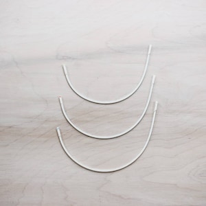 May include: Three white metal hoops of different sizes, stacked on top of each other.