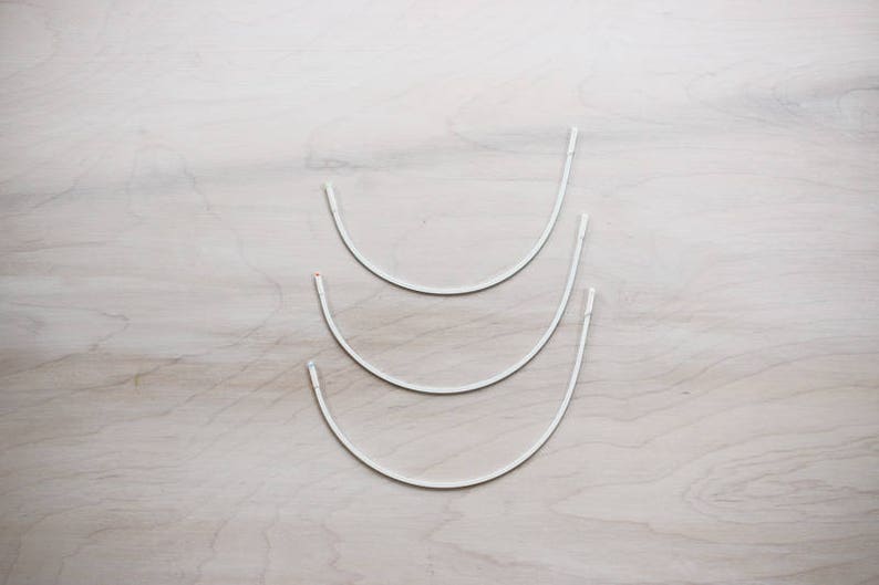 May include: Three white metal hoops of different sizes, stacked on top of each other.