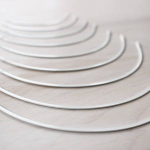 May include: A set of ten white metal boning for sewing projects. The boning is arranged in a fan shape, with the largest piece at the bottom and the smallest piece at the top.