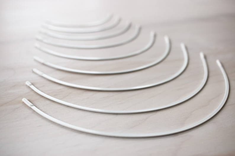 May include: A set of ten white metal boning for sewing projects. The boning is arranged in a fan shape, with the largest piece at the bottom and the smallest piece at the top.