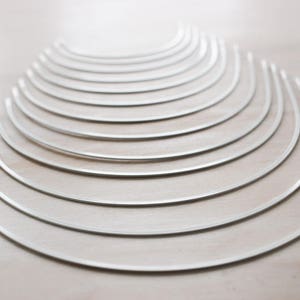 May include: A set of 15 silver metal hoops, arranged in a graduated size pattern, with the largest hoop at the bottom and the smallest hoop at the top.