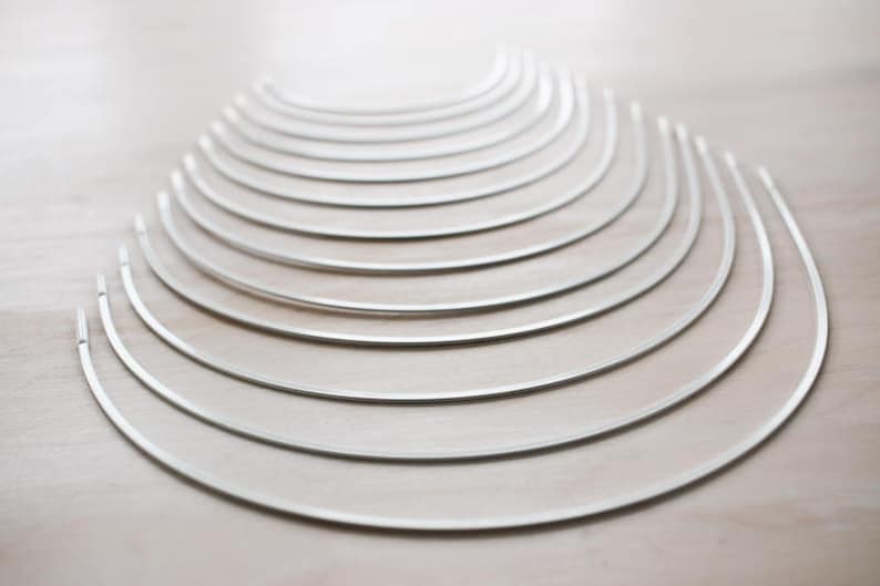 May include: A set of 15 silver metal hoops, arranged in a graduated size pattern, with the largest hoop at the bottom and the smallest hoop at the top.