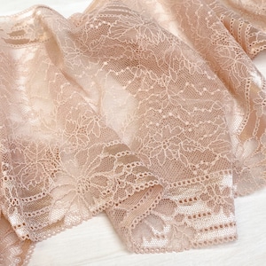 May include: A close-up of delicate, peach-colored lace fabric with a floral pattern. The lace is soft and sheer, with a subtle shimmer.
