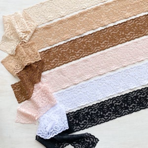 May include: Assortment of six different lace trims in various colors, including white, black, brown, pink, and beige. The lace trims are arranged in a row, with the black lace trim at the bottom.