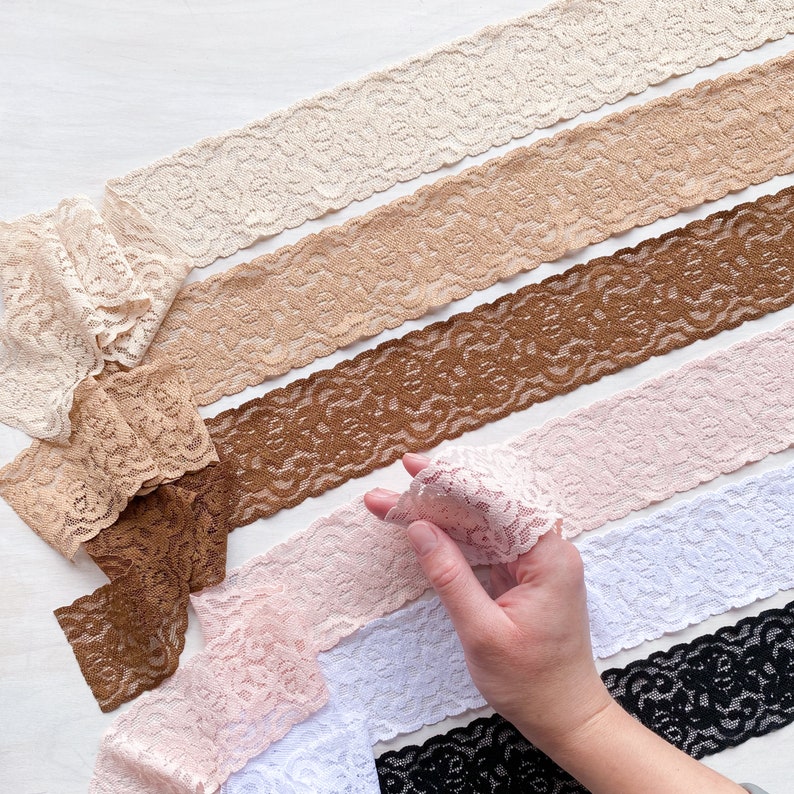 May include: Assortment of six different lace trims in various colors, including white, black, brown, beige, and pink. The lace trims have a delicate floral pattern and are arranged in a fan shape.