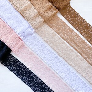 May include: Assortment of lace trim in black, pink, white, beige, and brown. The lace trim is delicate and has a floral pattern.