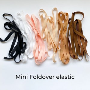 May include: Assortment of mini foldover elastic in black, white, peach, beige, and brown colors.