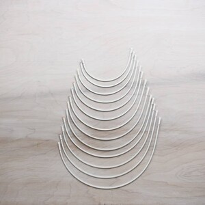 May include: A set of 10 silver-colored metal hoops of varying sizes, arranged in a pyramid shape on a light wood surface.