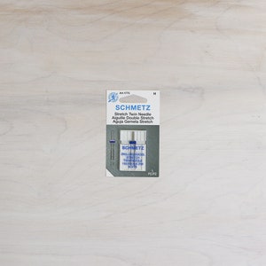 Pu&ograve; includere: Un pacchetto di aghi gemelli elastici Schmetz, misura 130/7055 2/1 40/75. La confezione &egrave; blu e bianca e riporta il testo "Schmetz Stretch Twin Needle".