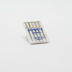 May include: A clear plastic package of five silver sewing needles labeled "SCHMETZ STRETCH 130/705 H-S 75/11"