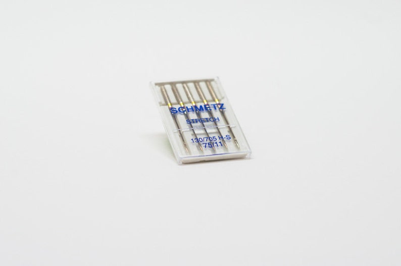 May include: A clear plastic package of five silver sewing needles labeled "SCHMETZ STRETCH 130/705 H-S 75/11"