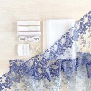 May include: A collection of white sewing supplies and blue butterfly lace. The lace features intricate butterfly designs and floral accents. Included are white ribbons, fabric, and a small metal ring.