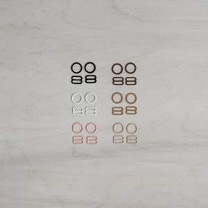 May include: A set of six bra strap adjusters in four different colours: black, white, light pink, and brown. Each set includes two rings and two sliders.