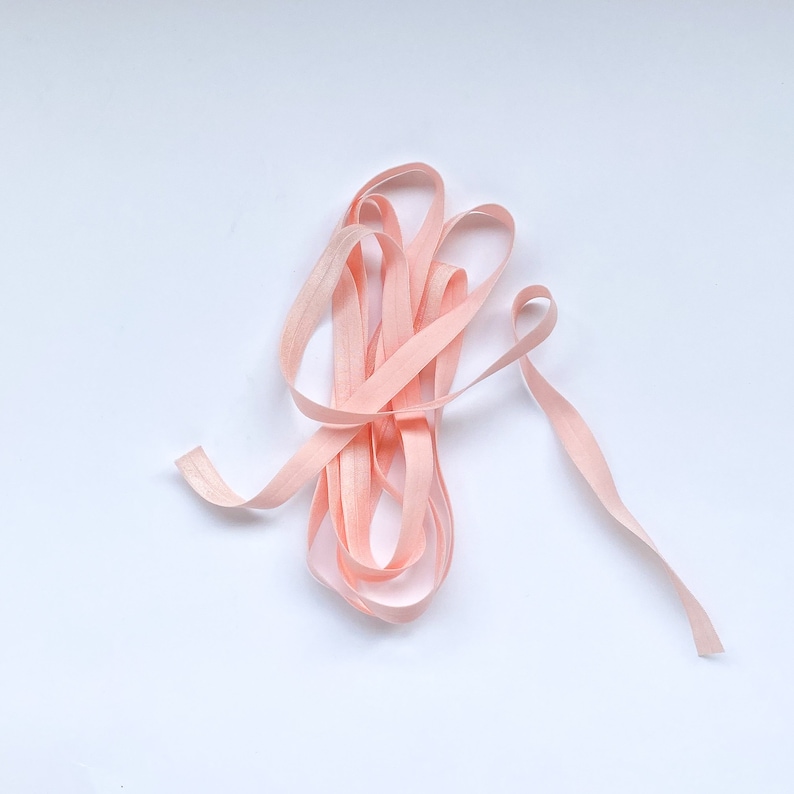 May include: A close-up of a pink elastic ribbon, coiled and ready for use in crafting or sewing projects.