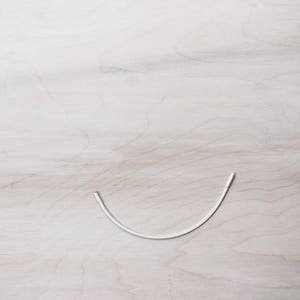 May include: A white wire bent into a U-shape on a light wood surface.