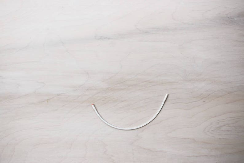 May include: A white wire bent into a U-shape on a light wood surface.