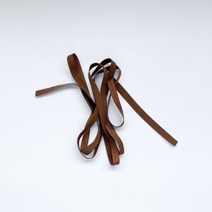 May include: A brown elastic band, folded and twisted, on a white background.