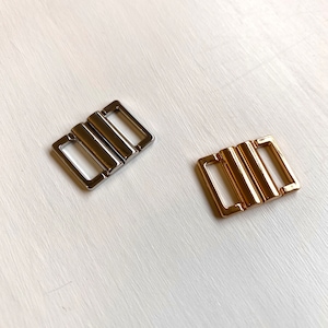 May include: Two metal bra clasps, one silver and one gold. Both clasps have three rows of metal.