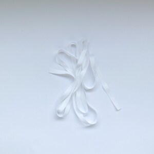 May include: A white elastic band, folded and twisted, on a white background.