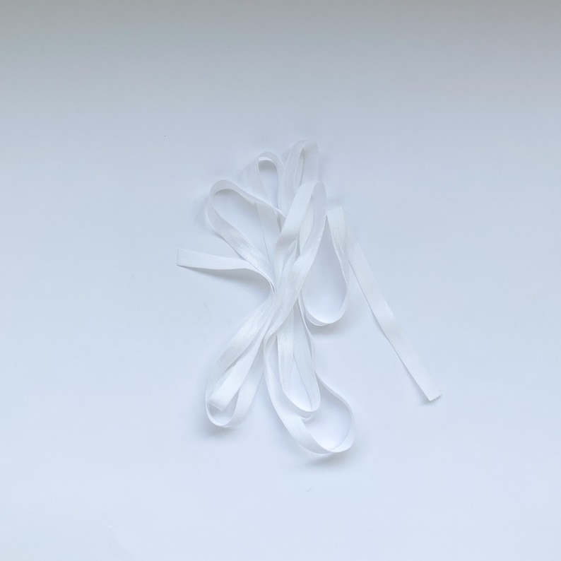 May include: A white elastic band, folded and twisted, on a white background.