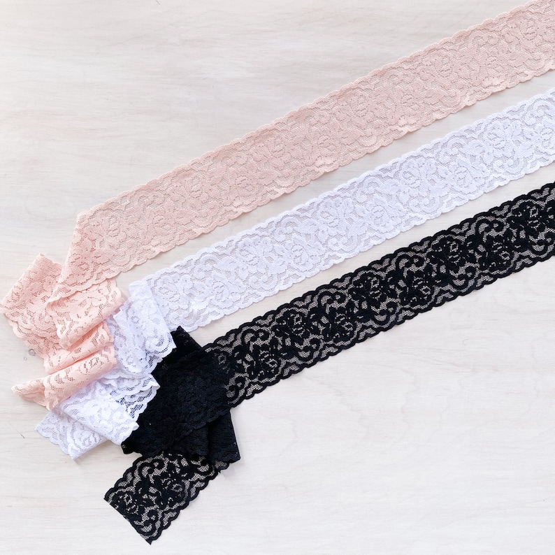 May include: Three different lace trims in pink, white, and black. The lace trims are delicate and have a floral pattern.