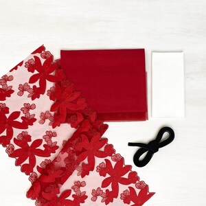Könnte beinhalten: Roter Stoff mit floraler Spitzenborte, ein quadratisches Stück roten Stoffes, ein quadratisches Stück weißen Stoffes und ein schwarzes Band.