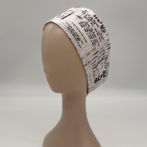 May include: White headband with black handwritten text and the letters "AC/DC" visible. The fabric appears to be cotton or a similar material. The headband is displayed on a mannequin head.