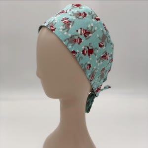 May include: A light blue surgical scrub cap featuring a repeating pattern of sock monkeys in red, gray, and white. The cap is tied at the back with matching fabric ties. The cap is designed to be worn in a medical setting.