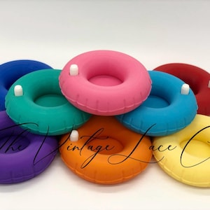 May include: A collection of colorful, miniature inflatable rings in shades of blue, green, pink, red, purple, orange, and yellow. Each ring has a small white detail. The Vintage Lace Co. logo is across the image.