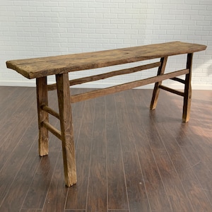 May include: A rustic wooden console table with a long, rectangular top and a simple, sturdy frame. The table is made of reclaimed wood and has a natural, weathered finish.