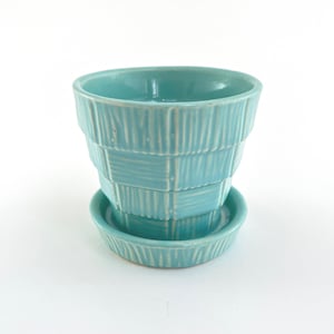 May include: A turquoise ceramic planter with a matching saucer. The planter has a textured, stacked design. The round saucer has a ribbed pattern. The planter is suitable for small plants and succulents.