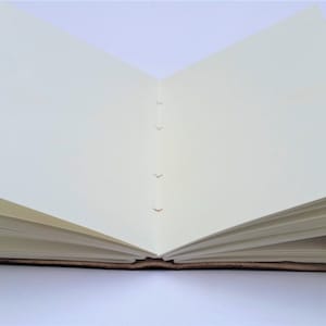 May include: An open, handmade journal with cream-colored pages. The journal's spine is visible, showing the binding stitches. The cover appears to be a dark brown, possibly leather, with a textured finish. The pages are blank and ready for writing or sketching.