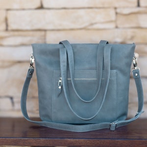 Handmade Italian leather tote with open and zipped exterior pockets, top zipper and long strap in avio color.