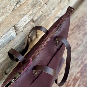 Handmade large tote bag in full-grain Italian leather, shown in Bordo hue, with exterior pocket and natural suede interior. Features optional top YKK zipper closure — a stylish work or travel purse for her.