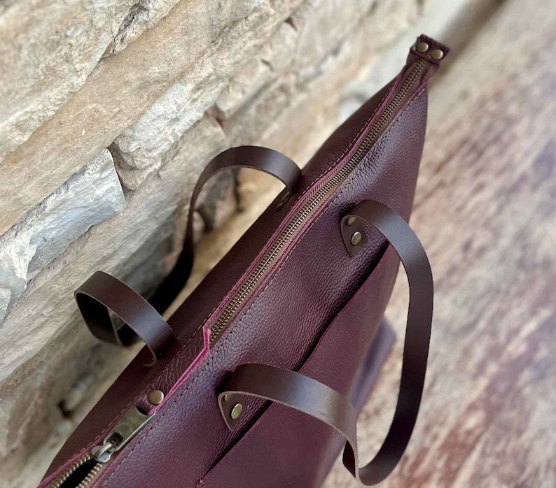 Handmade large tote bag in full-grain Italian leather, shown in Bordo hue, with exterior pocket and natural suede interior. Features optional top YKK zipper closure — a stylish work or travel purse for her.