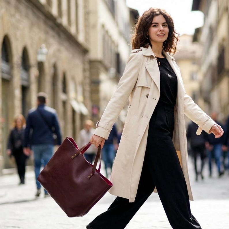 May include: A large, deep burgundy leather tote bag with thin brown handles and a vibrant pink interior lining. The bag features a structured rectangular shape with visible stitching at the handle attachments and a smooth, matte finish exterior.