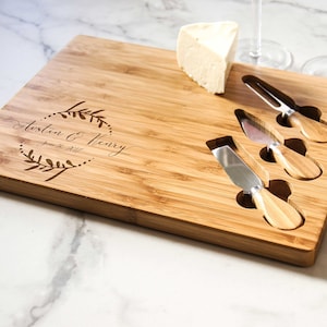 May include: A personalized bamboo cheese board with four cheese knives and a block of cheese. The board is engraved with the text "Austin & Henry June 18, 2017".