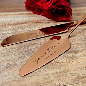 May include: Rose gold wedding cake knife and server set with the names "Yvan & Rebecca" and the date "EST. 2025" engraved on the handles.