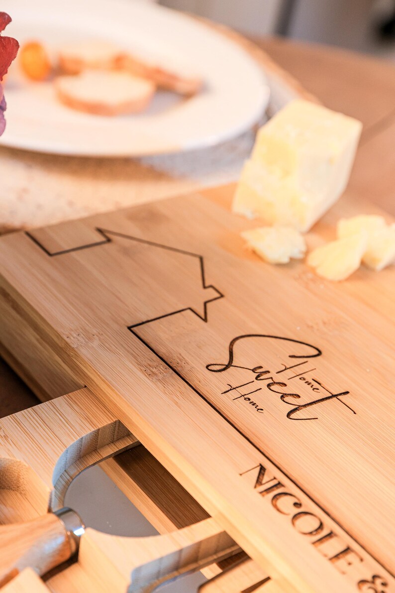 May include: A wooden chopping board with a drawer for storing knives. The board is engraved with the text "One Sweet Home" and a house design. The board also has the name "Nicole &" engraved on it.