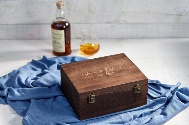 May include: A dark brown wooden box with a hinged lid and brass clasps. The lid is engraved with the text "Gwen & Rebecca Est. 2022".