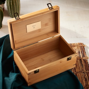 May include: An open wooden box with a brass latch and a small brass plaque that reads "Enjoy it!"  The box is made of light brown bamboo wood and has a natural wood finish.