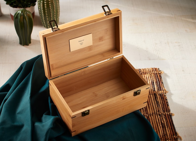 May include: An open wooden box with a brass latch and a small brass plaque that reads "Enjoy it!"  The box is made of light brown bamboo wood and has a natural wood finish.