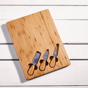 May include: A wooden cheese board with four stainless steel cheese knives. The board has slots to hold the knives.