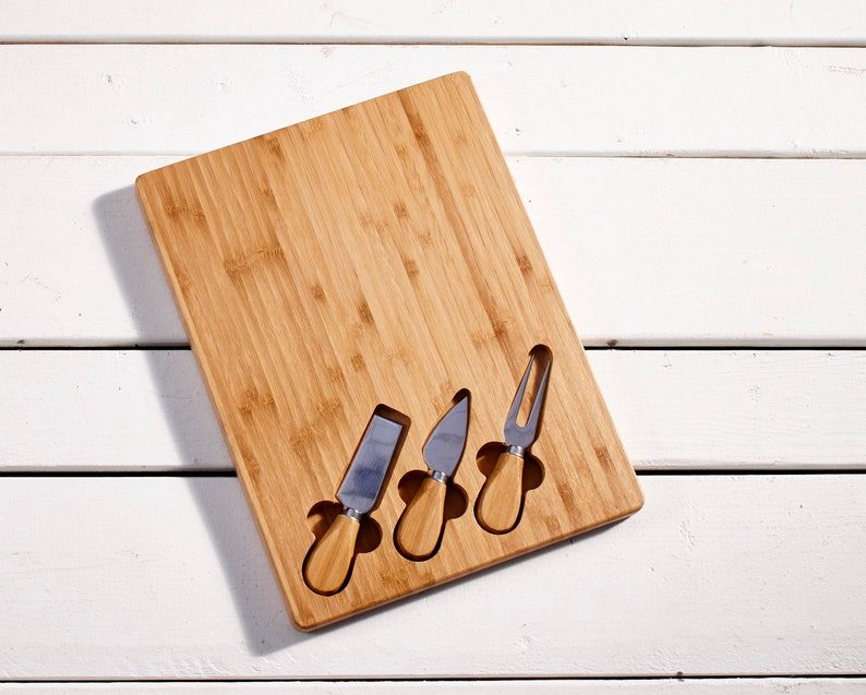 May include: A wooden cheese board with four stainless steel cheese knives. The board has slots to hold the knives.